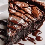 Gooey brownie pie topped with chocolate drizzle on a white plate