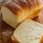 Freshly baked sourdough sandwich bread loaf on a wooden cutting board.