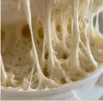 Homemade sourdough starter in a glass jar with fresh ingredients