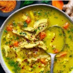Bowl of anti-inflammatory turmeric chicken soup garnished with herbs.