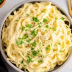 Bowl of creamy dairy-free Alfredo sauce with fresh herbs and pasta