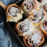 Delicious gluten-free cinnamon rolls topped with icing on a baking sheet.
