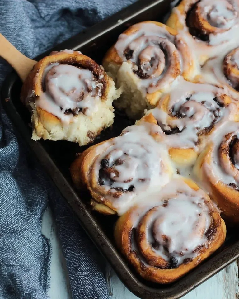 Delicious gluten-free cinnamon rolls topped with icing on a baking sheet.