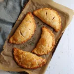 Gluten-free Cornish pasties filled with savory ingredients on a wooden table